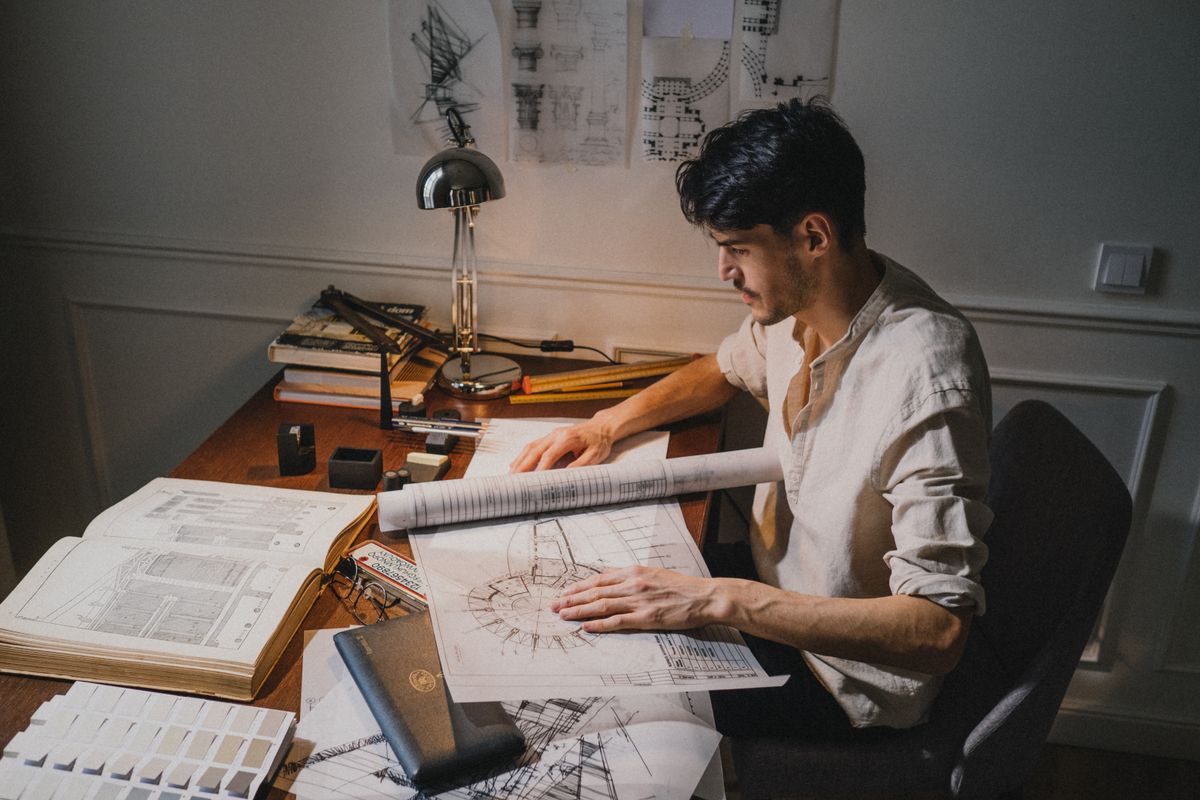 Person reviewing a rolled architectural drawing at a desk under a lamp