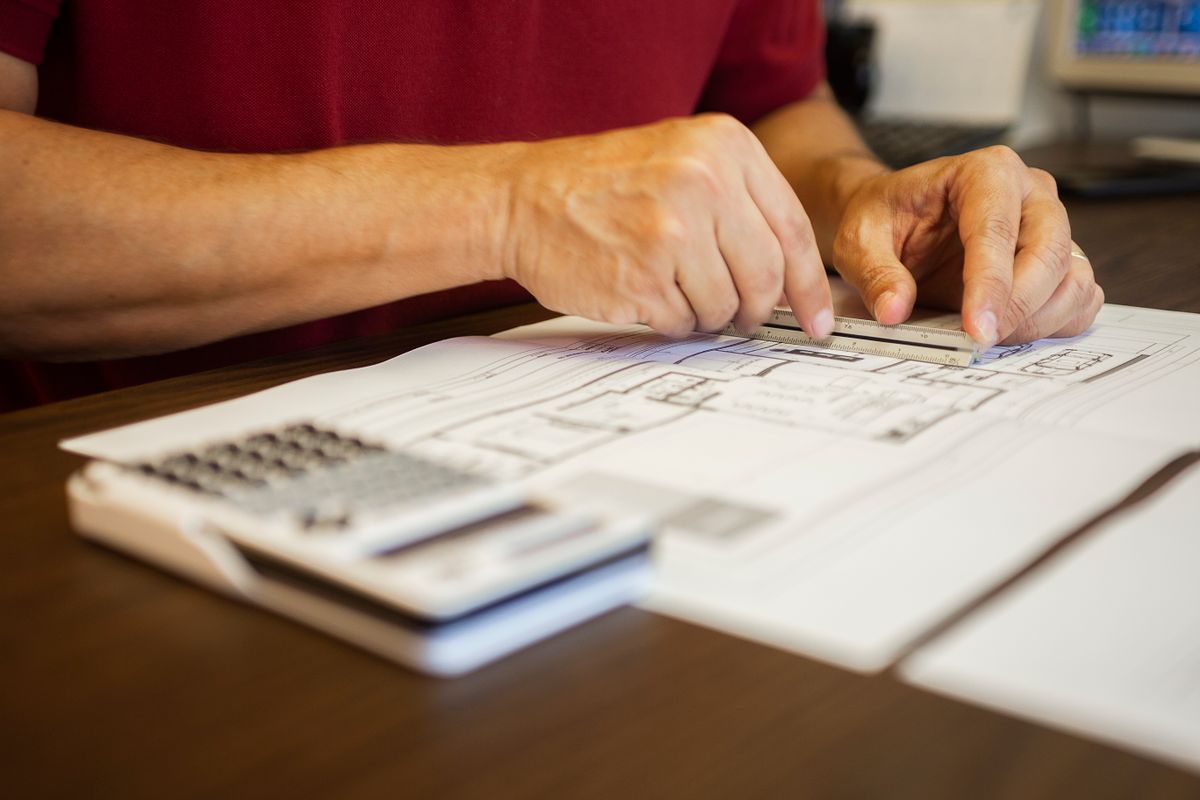 Hands using a calculator next to an architectural blueprint on a desk